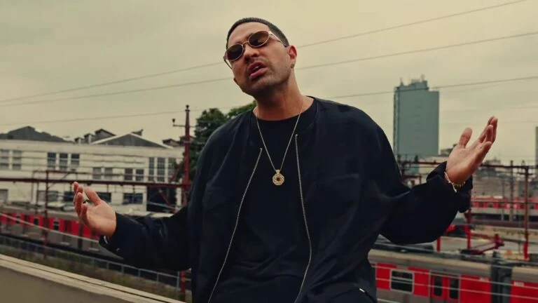 Rapper canta em cena do clipe Poetas no Topo DEMOCRACIA, com trilhos de trem ao fundo